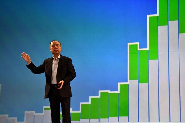 Masayoshi Son standing on a stage, in front of a backdrop with charts and graphs.