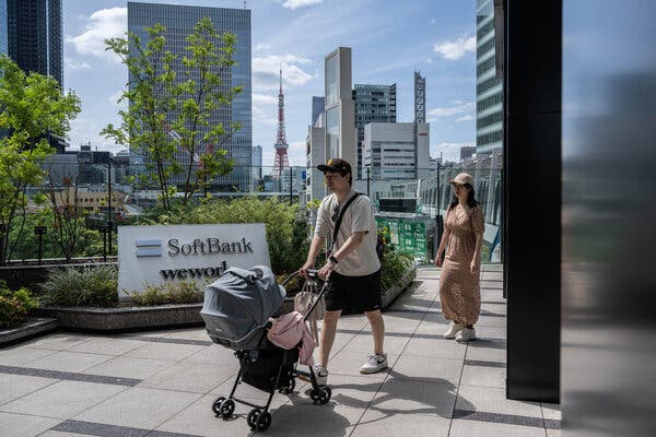 People walking with a pram, in front of a sign that says SoftBank. 