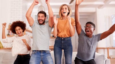 Excited group of friends sitting on sofa watching sports on TV and celebrating.